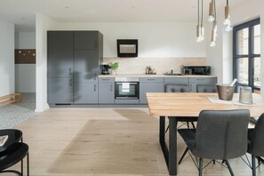 A modern kitchen with grey cabinets, a wooden dining table, and pendant lights. - Coastal Suite North | Directly on the waterfront (Greetsiel)