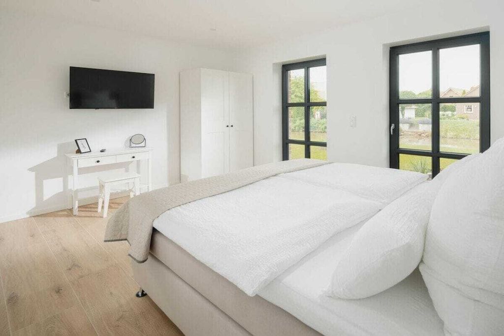 A bedroom with a bed, a desk, a television, and a window.