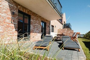 A modern building with a brick facade, a balcony with a metal railing, and lounge chairs outside. - Coastal Suite North | Directly on the waterfront (Greetsiel)