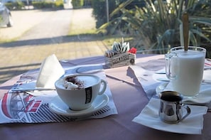 Et bord med en kop kaffe, et glas mælk og en lille metal kop, sandsynligvis med sukker eller sirup, samt en ske.