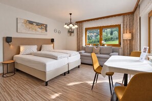 Een hotelkamer met twee bedden, een bank, een eettafel en uitzicht op het omliggende landschap.