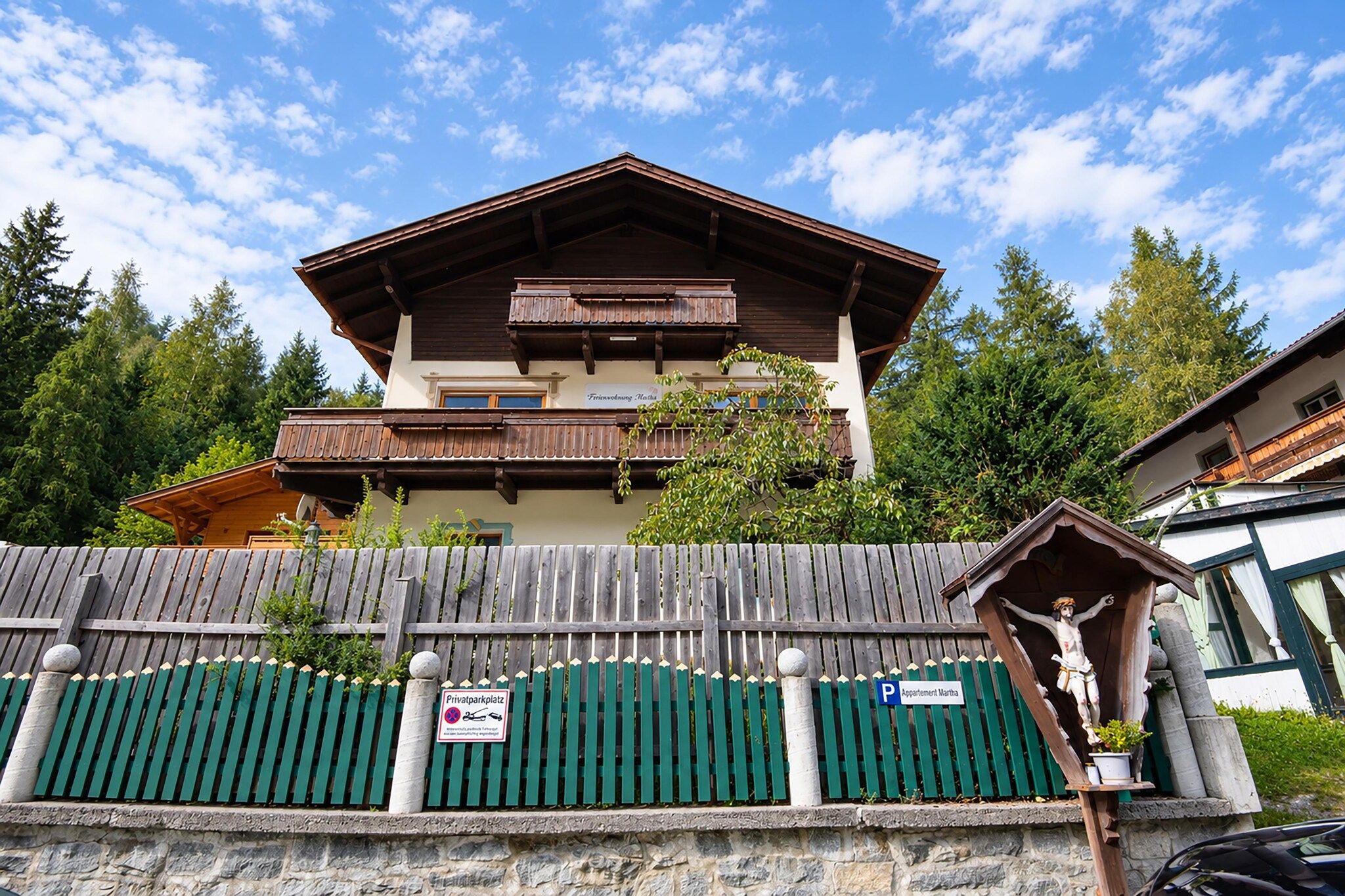 Un bâtiment de style chalet, doté d’un balcon, entouré d’une clôture en bois et d’arbres.