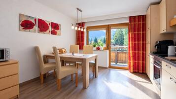 A modern kitchen with wooden cabinets, a dining area with a table and chairs, and a window with curtains.