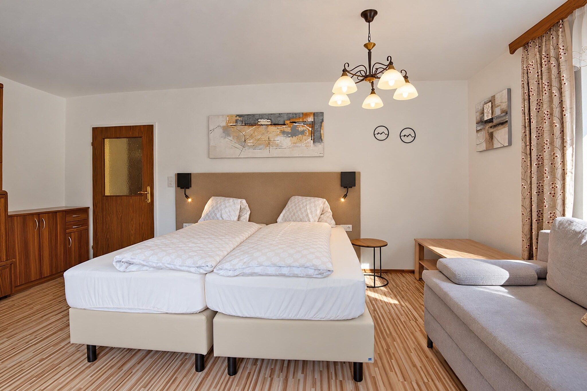 Un lit double avec une tête de lit, une table de chevet, un canapé, un plancher en bois et un lustre.