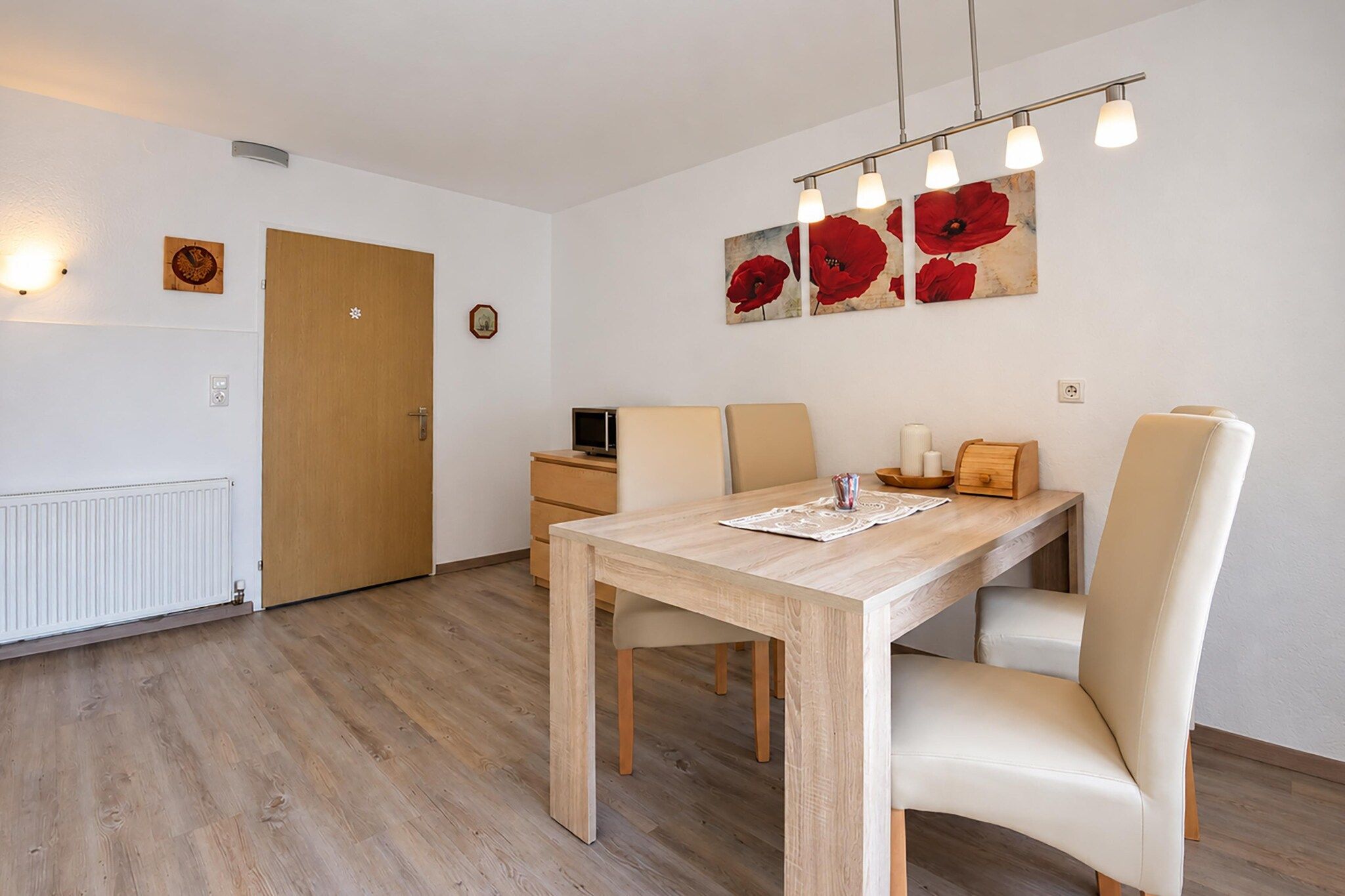 En matplats med ett träbord, beige stolar, ett litet sidobord och en väggmonterad lampa.