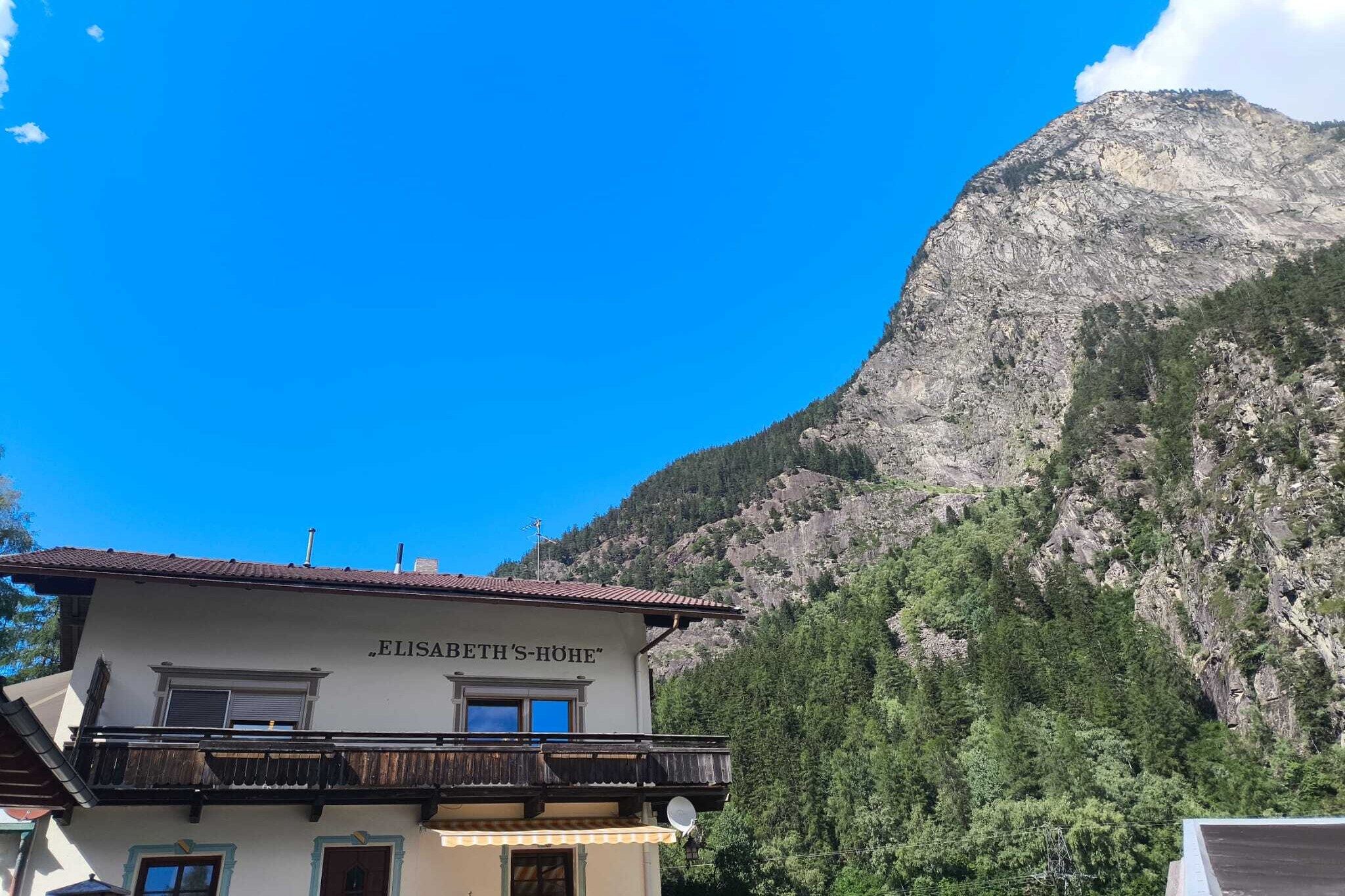 A building named 'ELISABETH'S-HÖHE' with a balcony, set against a mountainous backdrop.