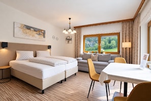 Een hotelkamer met een tweepersoonsbed, een slaapbank, een eettafel en uitzicht op groen buiten de ramen.