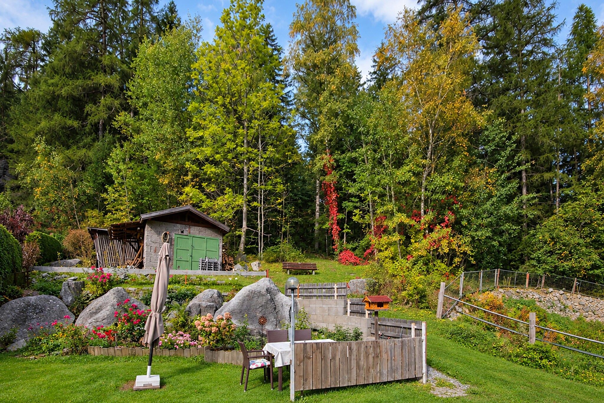 A rustic cabin with a green door, surrounded by a garden with large rocks and flowering plants.