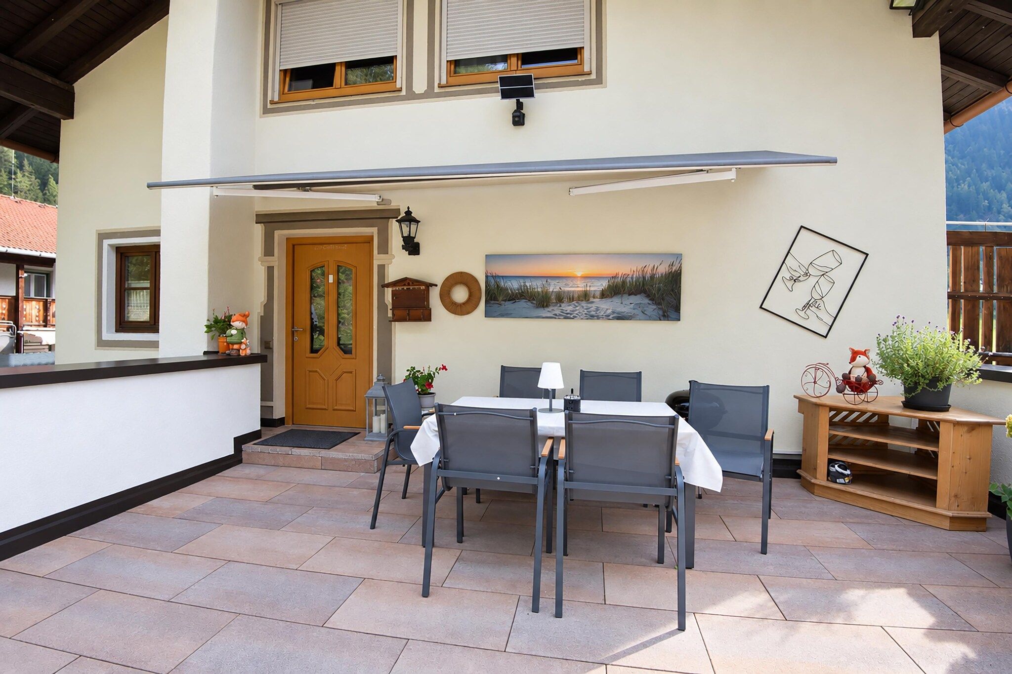 Une terrasse extérieure avec une table et des chaises, une porte en bois et un tableau accroché au mur.