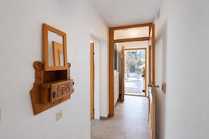 Een gang met een houten kast en spiegel, die uitkomt op een besneeuwde omgeving.