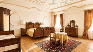 Een kamer met een groot bed, een houten dressoir, een ronde tafel met stoel, en een kamerbreed tapijt met dessin.