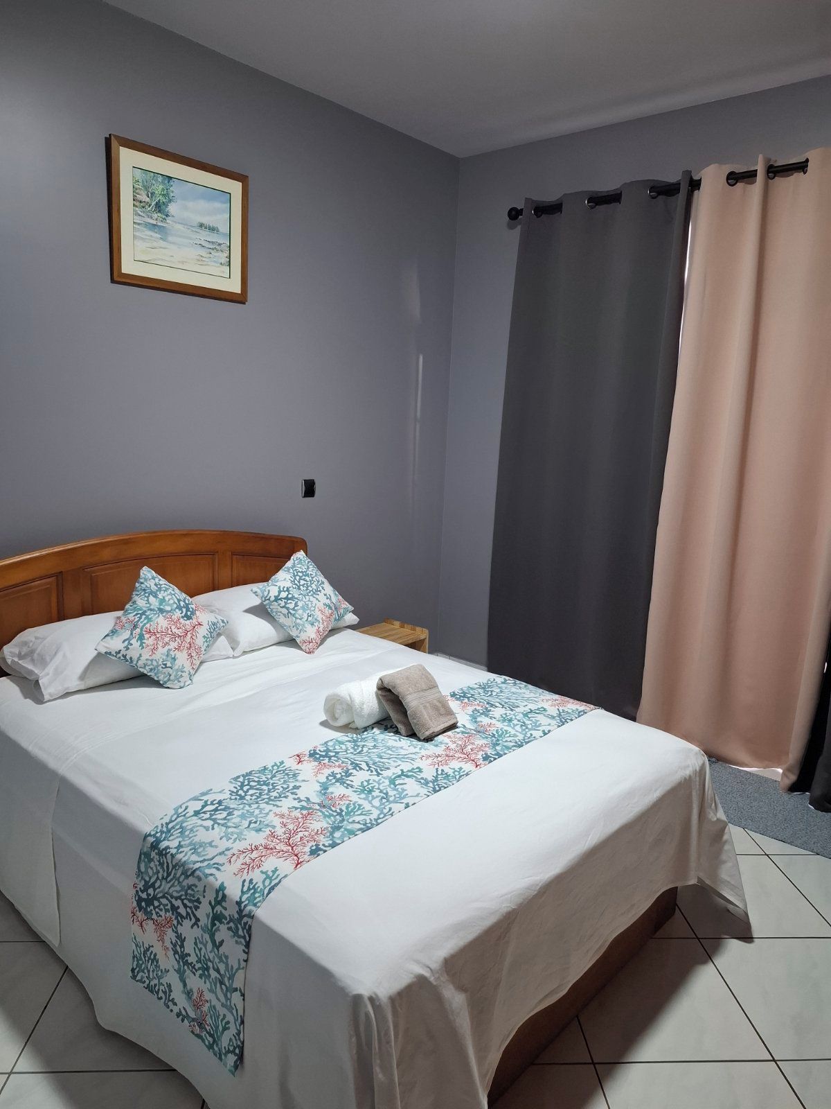 A neatly made bed with a floral bedspread, a wooden headboard, and a framed picture on the wall.