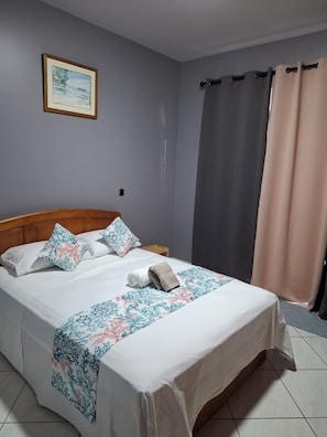 Un lit bien fait, recouvert d’une couvre-lit à motifs floraux, avec une tête de lit en bois et un tableau encadré accroché au mur.