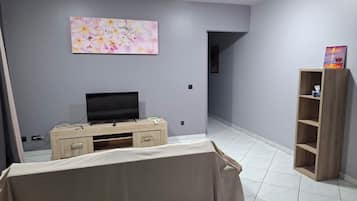 Habitació amb televisió sobre un suport de fusta, un quadre a la paret i una prestatgeria de fusta amb un llibre.