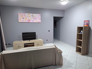 Une pièce avec un téléviseur posé sur un meuble en bois, un tableau accroché au mur et une étagère en bois sur laquelle se trouve un livre.