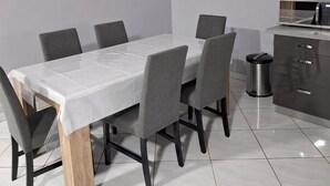 Un comedor moderno con una mesa blanca, sillas grises, un ventilador de techo y una zona de cocina con microondas.