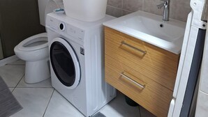 Un baño pequeño con lavadora, inodoro y lavamanos con gabinete de madera.