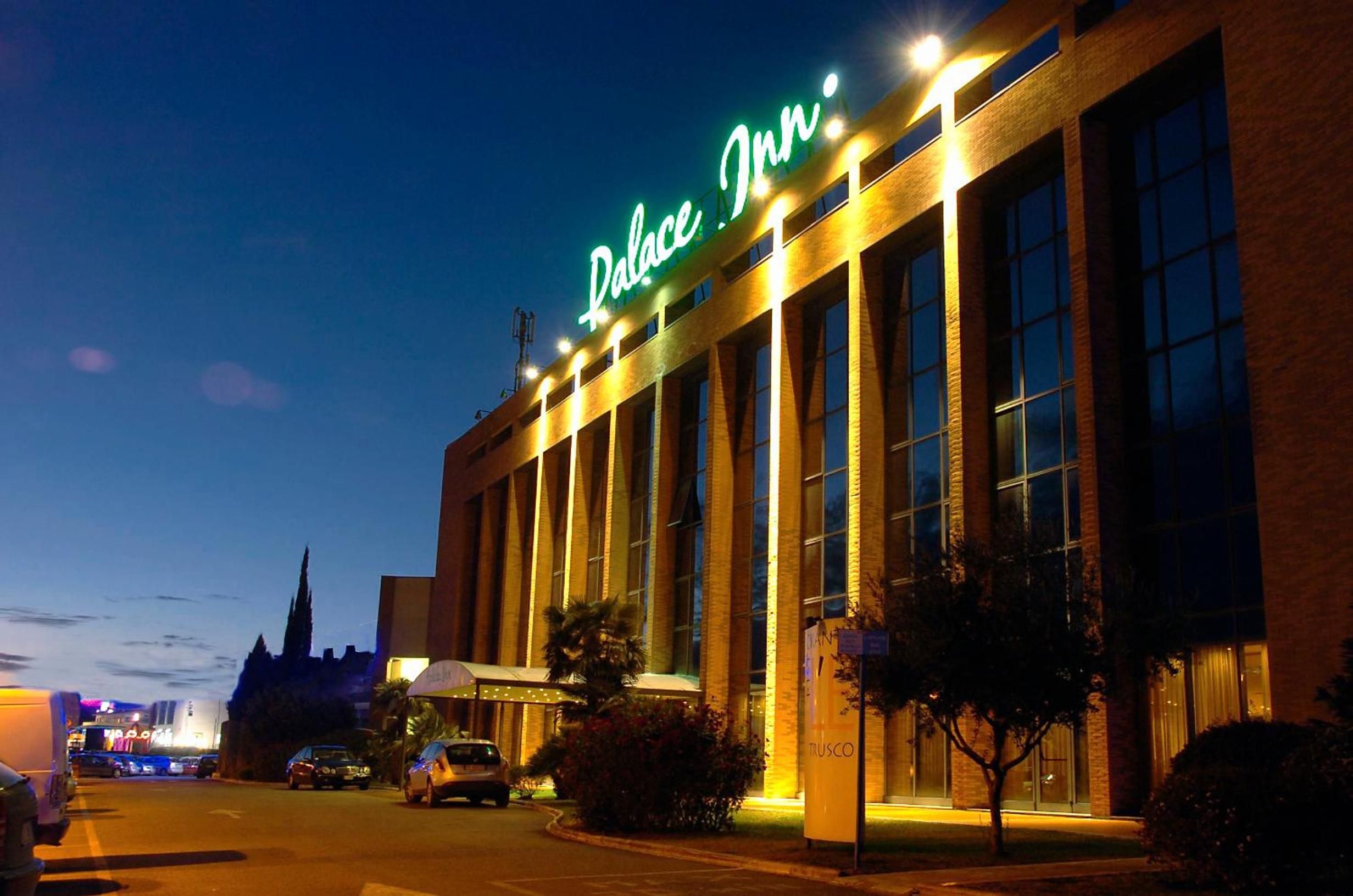 A hotel with a prominent 'Palace Inn' sign, large windows, and a parking lot with cars.