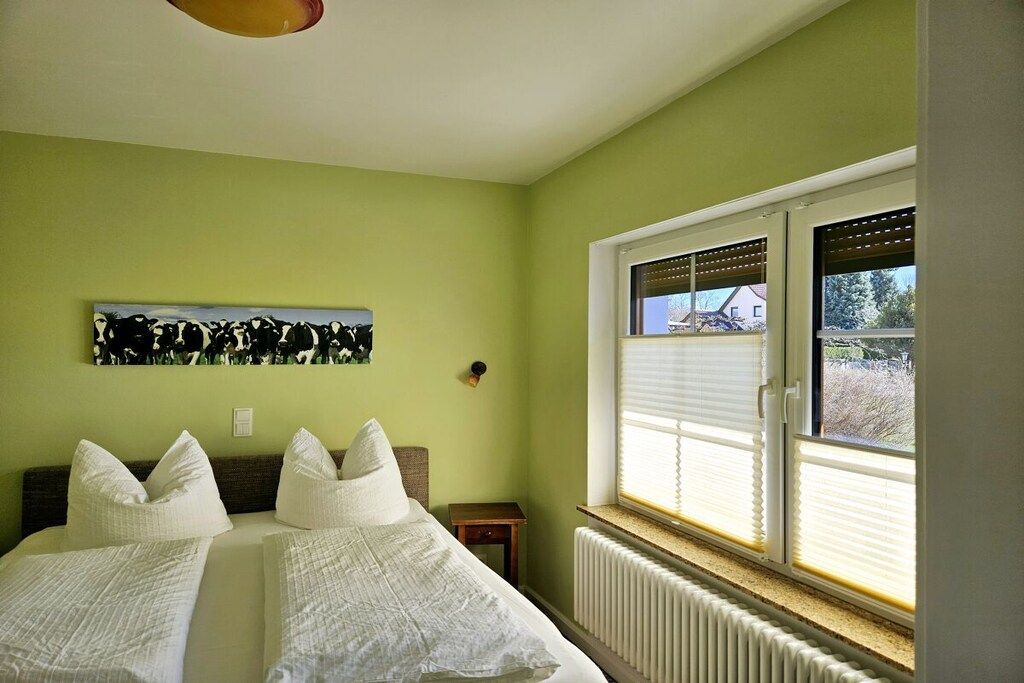 A room with two beds, a radiator, a window with blinds, and a painting on the wall.
