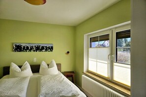 A room with two beds, a radiator, a window with blinds, and a painting on the wall. - Holiday apartment with 1 bedroom (Lübbenau\/Spreewald)