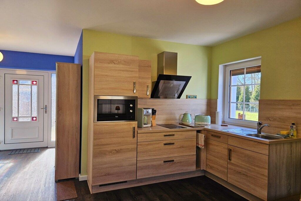 Une cuisine compacte avec des meubles en bois, un four à micro-ondes, une bouilloire et un évier.