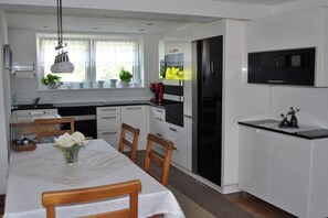 A modern kitchen with white cabinetry, a dining table with chairs, a black refrigerator, and a flat-screen TV mounted above the counter. - Holiday apartment with 1 bedroom (Gösselsdorf)