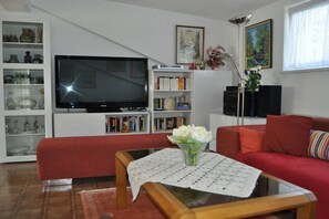 En stue med et fladskærms-tv, en reol, en rød sofa og et sofabord med en vase blomster.