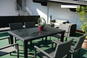 Een terras met een tafel, stoelen, een plant in pot en een trap.