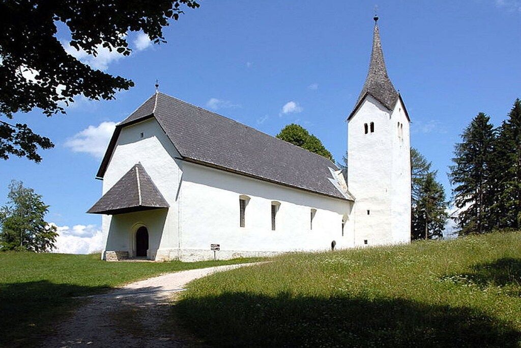 A church with a white exterior and a tall steeple, surrounded by greenery.