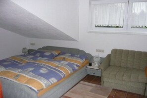 Een slaapkamer met een bed, een nachtkastje, een lamp, een raam met gordijnen en een bank.