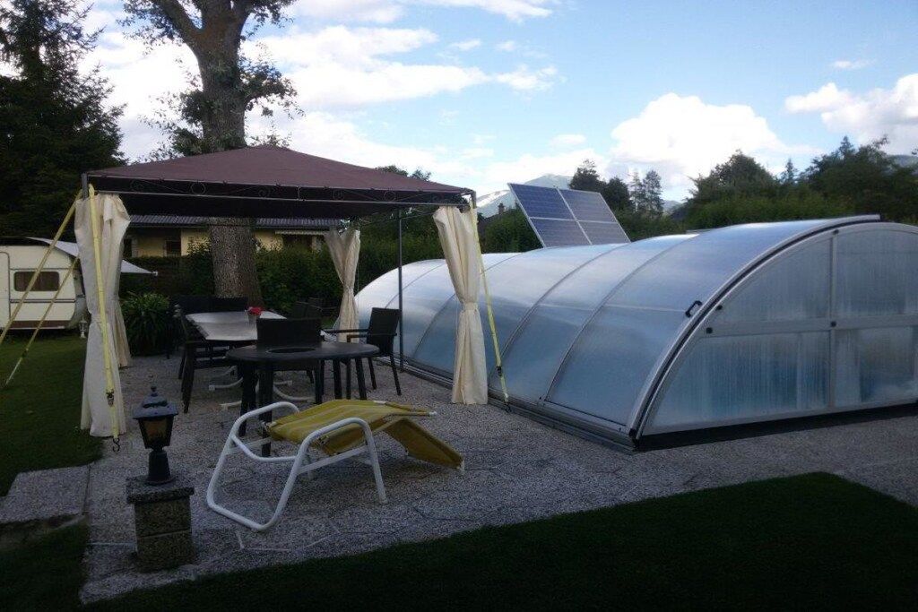 A greenhouse structure with a transparent roof, a covered seating area with a table and chairs, and a small lamp post.