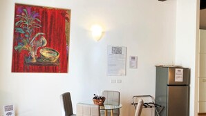 A dining area with a table and chairs, a painting on the wall, and a refrigerator.