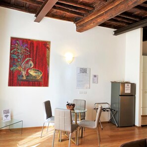 A dining area with a table and chairs, a painting on the wall, and a refrigerator.