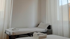 A room with two single beds, a wooden ceiling, and sheer curtains.