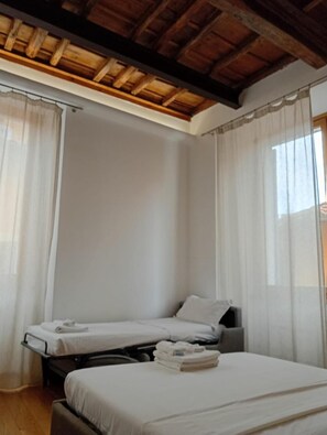 A room with two single beds, a wooden ceiling, and sheer curtains.