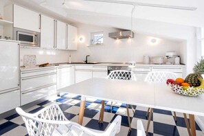A modern kitchen with white cabinetry, a central island, and a dining area with a checkered floor. - 3 (Sun deck) in Villa Fabiola (Ostseebad Binz)