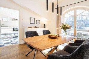 A modern dining area with a wooden table and chairs, a vase with flowers, and a view of the outdoors through large windows. - 3 (Sun deck) in Villa Fabiola (Ostseebad Binz)