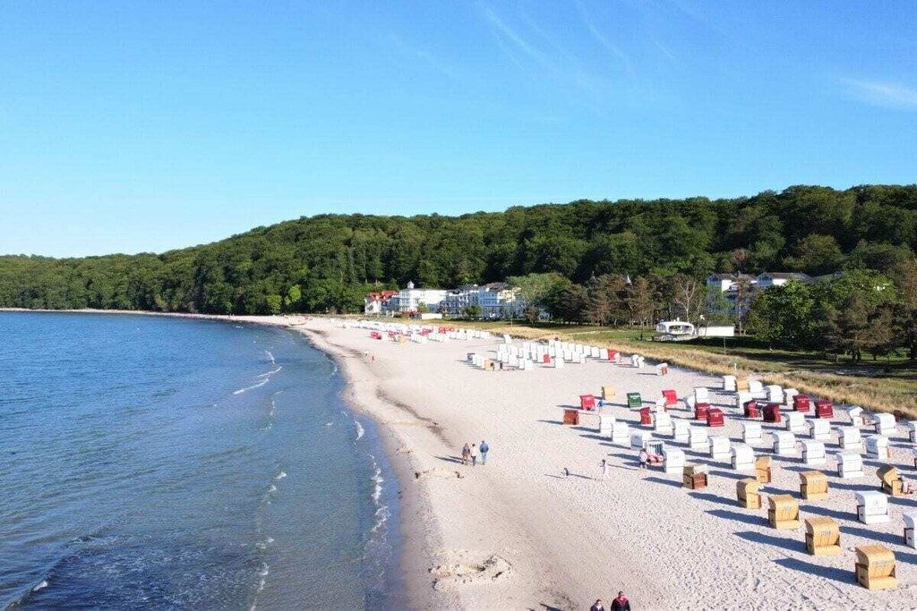 Ein Strand mit weißen und roten Liegen, einem Sandufer und einer bewaldeten Hügelkette im Hintergrund.