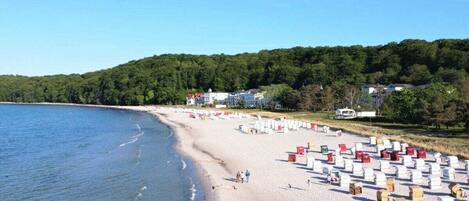 Une plage avec des chaises de plage blanches et rouges, un rivage sablonneux et, en arrière-plan, une colline boisée.