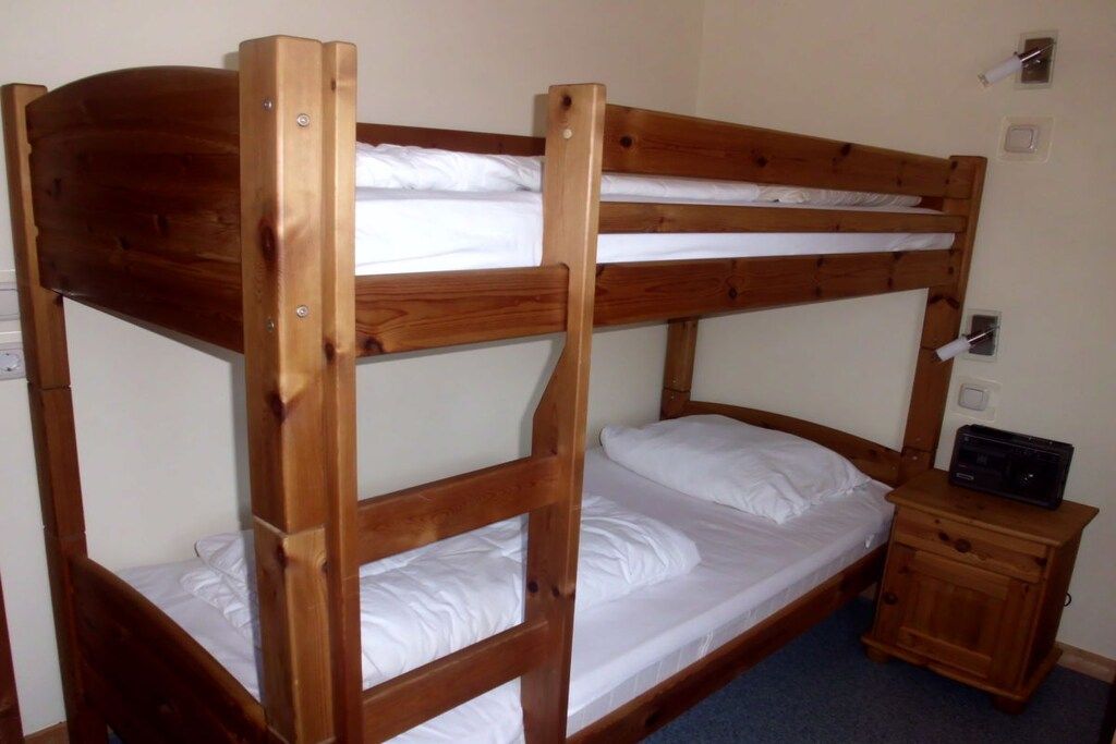 Un letto a castello con struttura in legno, biancheria bianca e un comodino in legno con una radio.