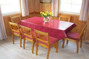 A dining area with a red table and wooden chairs, a vase with yellow flowers, and wooden paneled walls. - Swedish house with lake view (Userin)