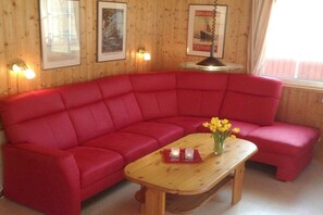 A red sofa with a wooden coffee table in front, a vase with yellow flowers, and framed pictures on the wall. - Swedish house with lake view (Userin)