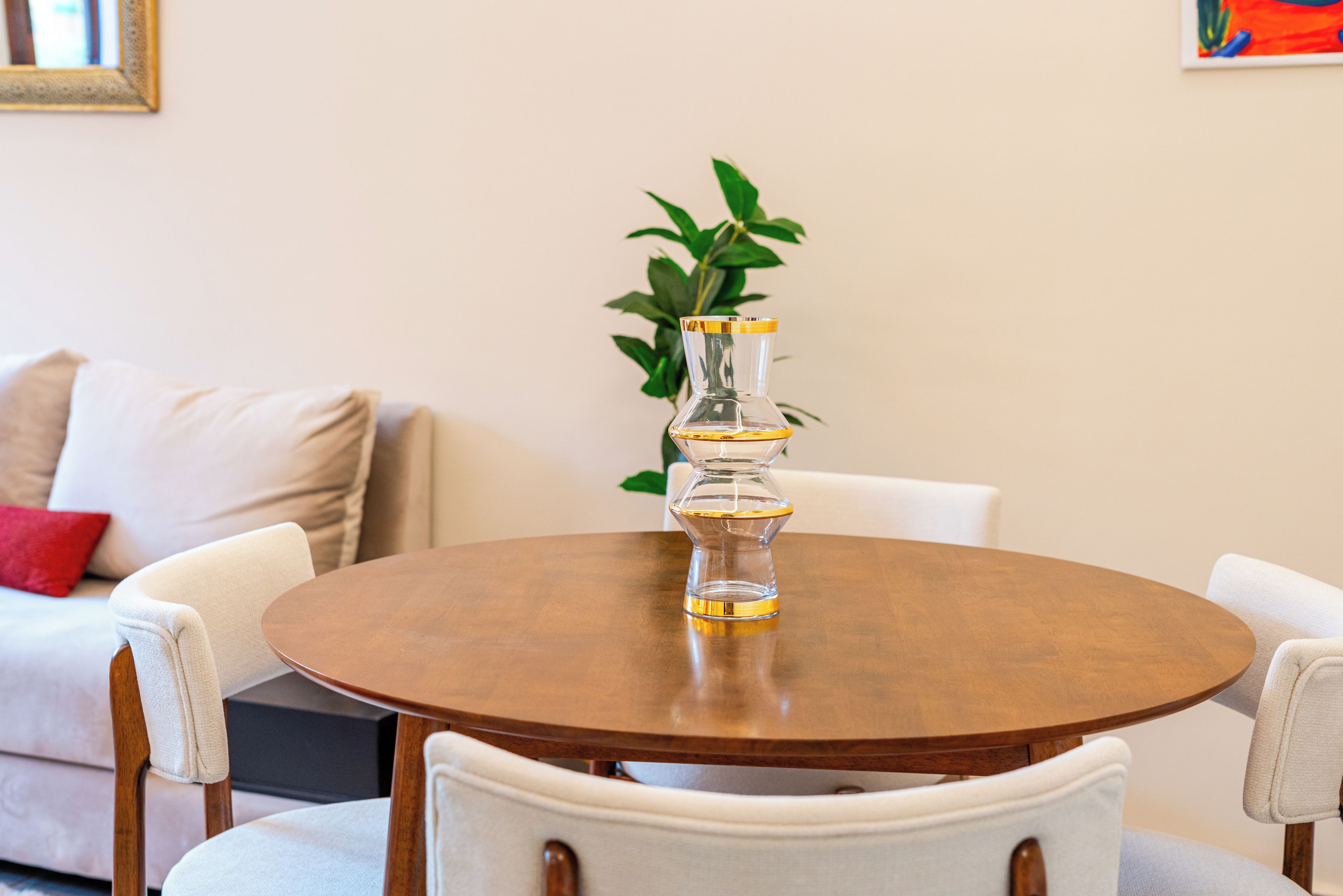 A round wooden table with a clear glass vase in the center, surrounded by four white upholstered chairs.