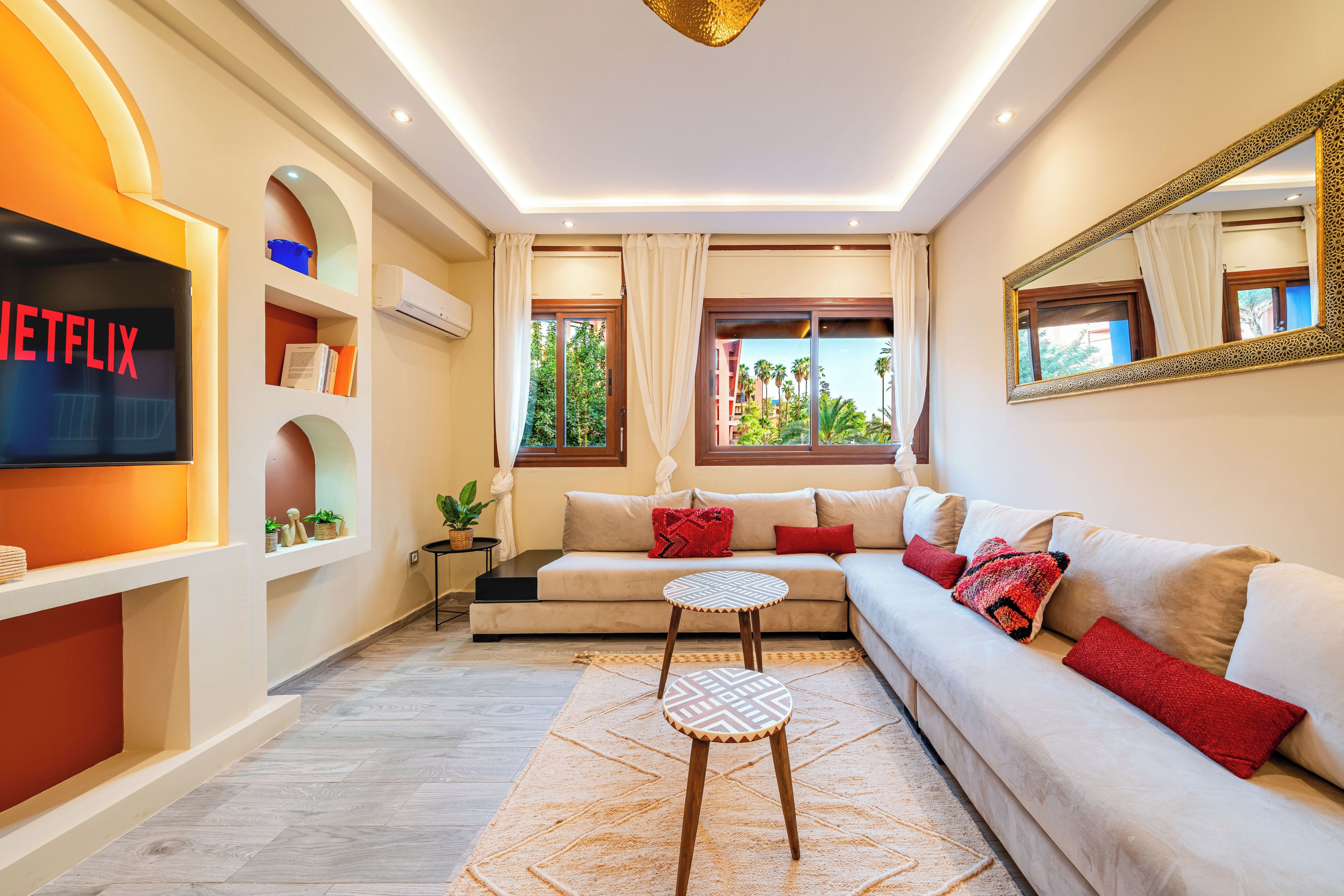 A modern living room with a sofa, a coffee table, a TV, and a large window with a view of greenery.
