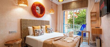 A modern hotel room with a large bed, a TV, and a balcony with a view of the city.