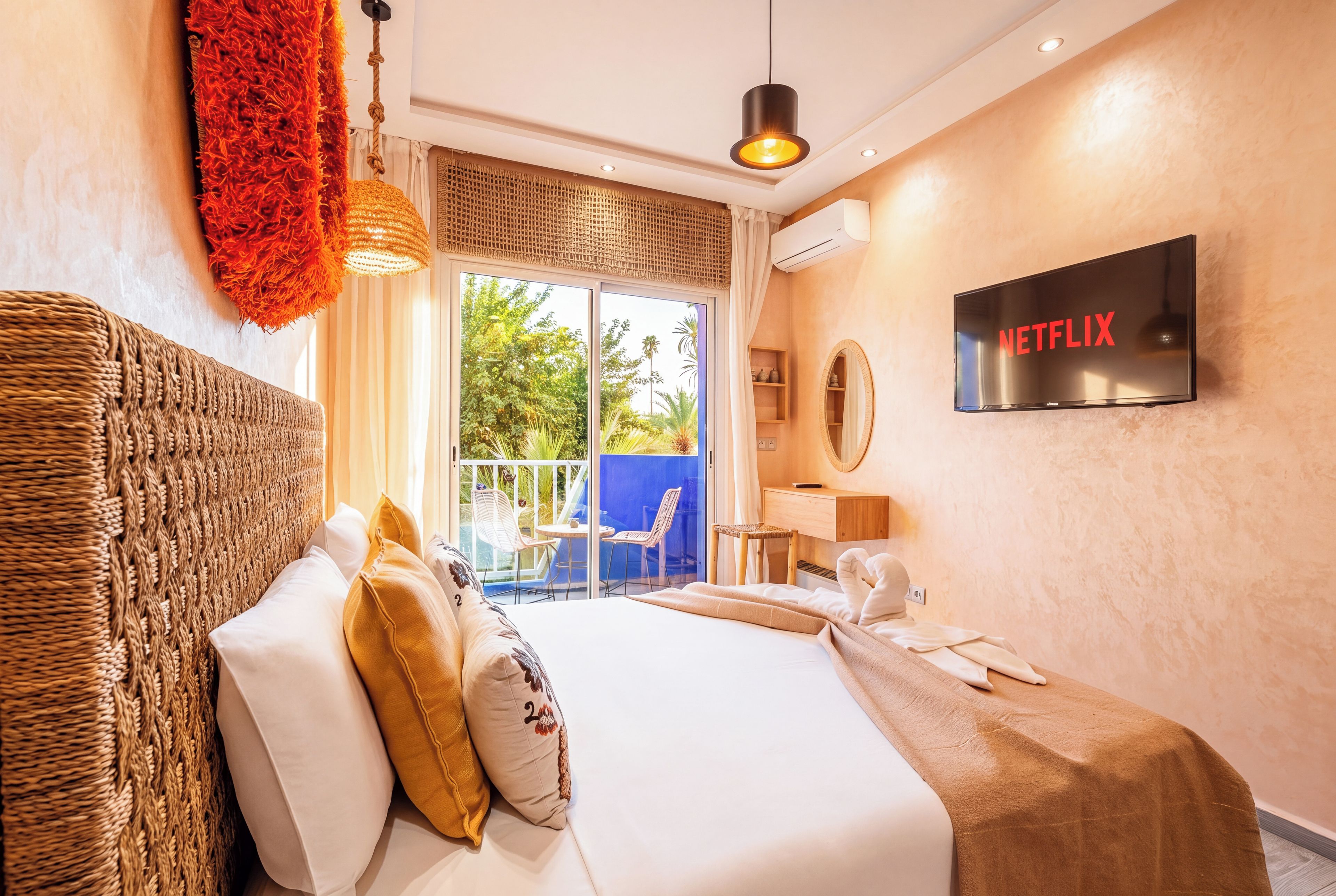 Quarto de hotel com cama, escrivaninha, cadeira, televisão e varanda com vista para o verde.