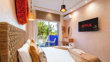 A hotel room with a bed, a television, a balcony with a view, and a wall-mounted air conditioning unit.