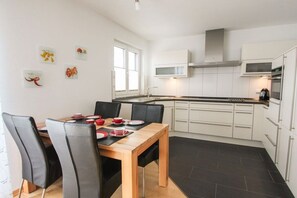 A modern kitchen with white cabinets, a wooden dining table, and black chairs. - Residence Margarete 1.12 (Ostseebad Binz)
