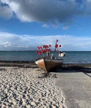 A boat with multiple red flags on a sandy beach next to a body of water. - Residence Margarete 1.12 (Ostseebad Binz)