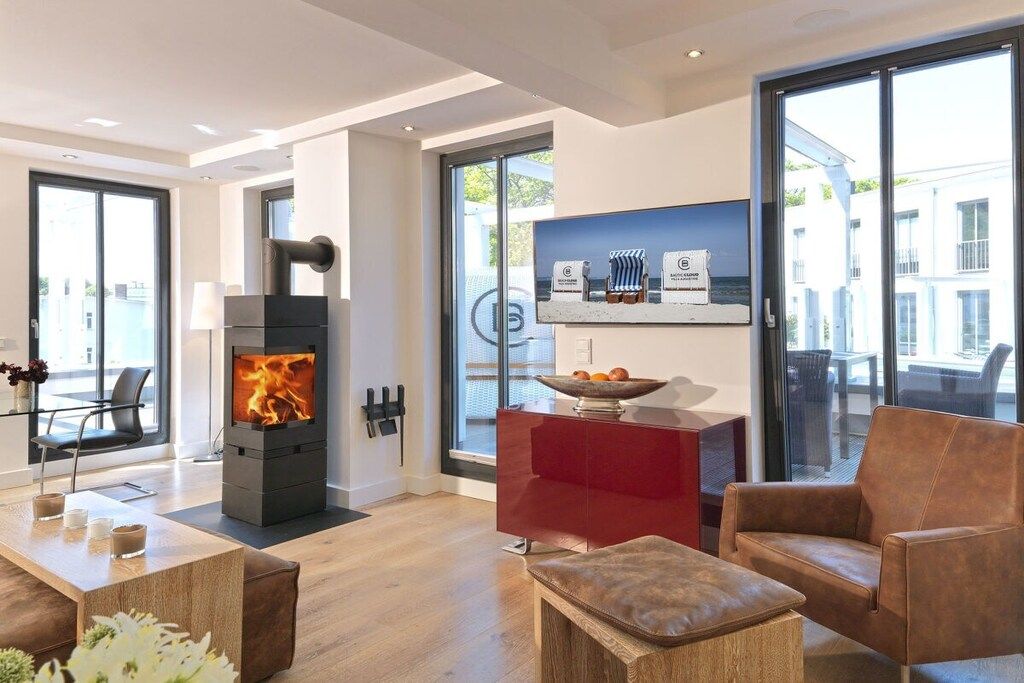 A modern living room with a wood-burning stove, a red cabinet, and a large window.